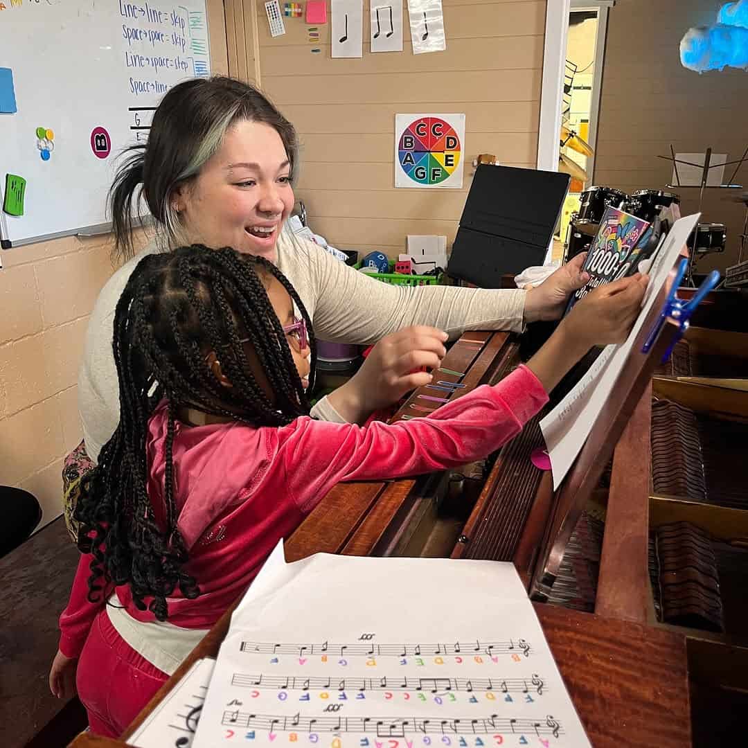 An instructor and a child sitting at a piano and learning.