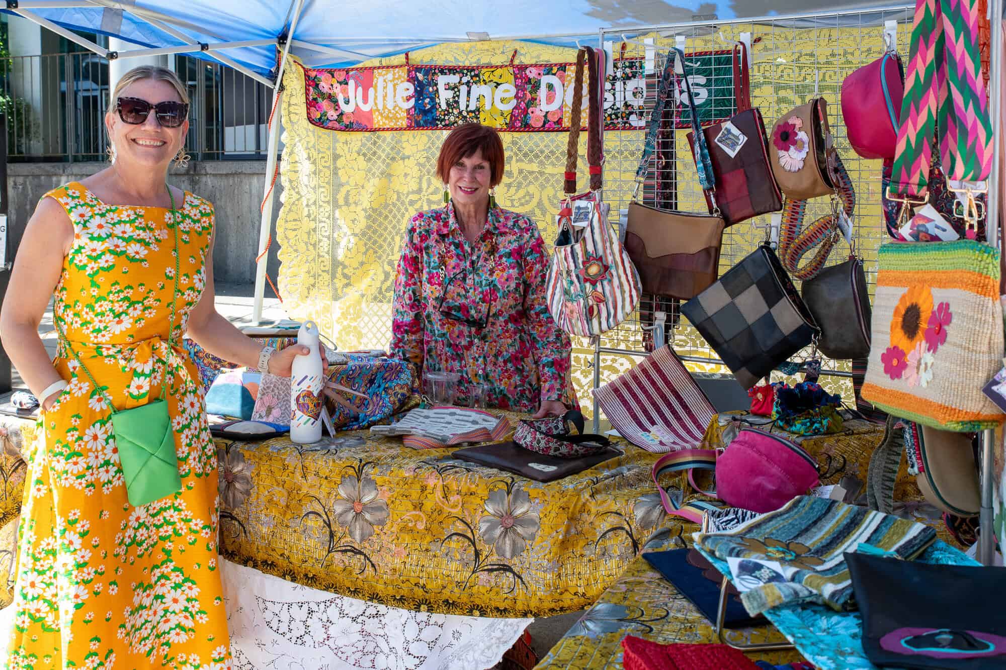 A photo of two women at a vendor stand selling bags.