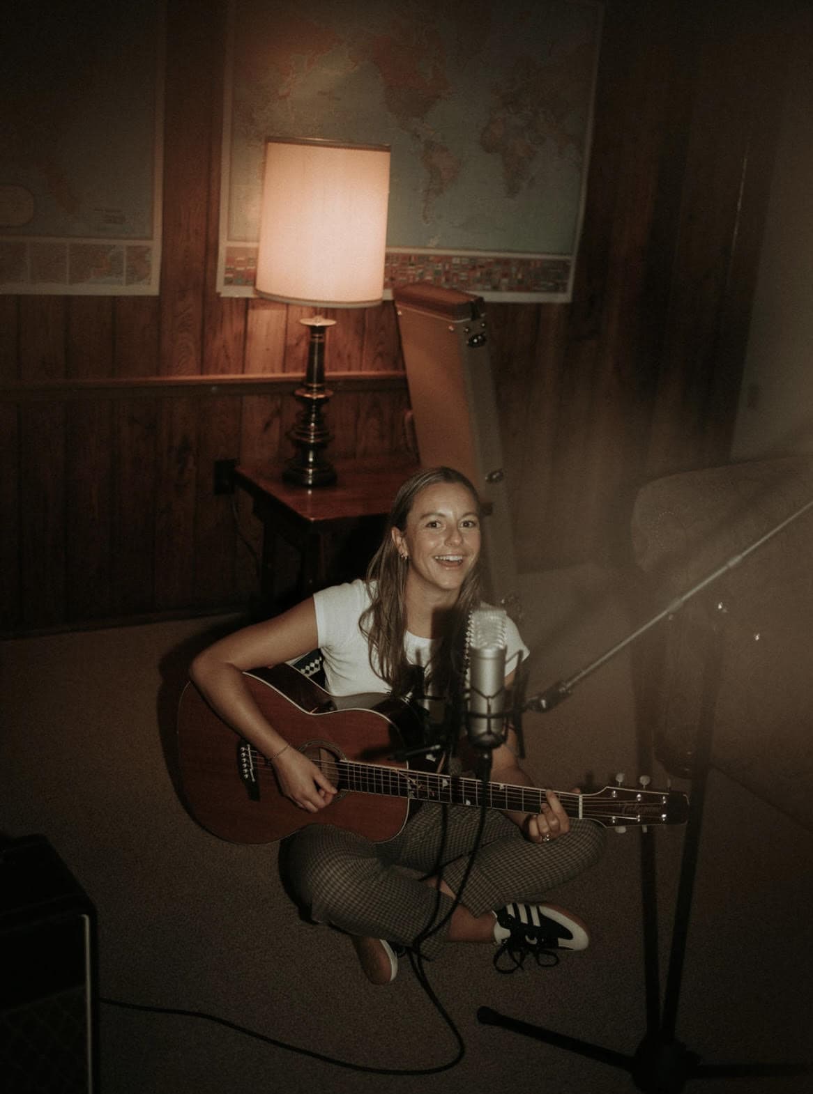 A photo of Kelly McCafferty playing an acoustic guitar and singing while sitting on the floor.