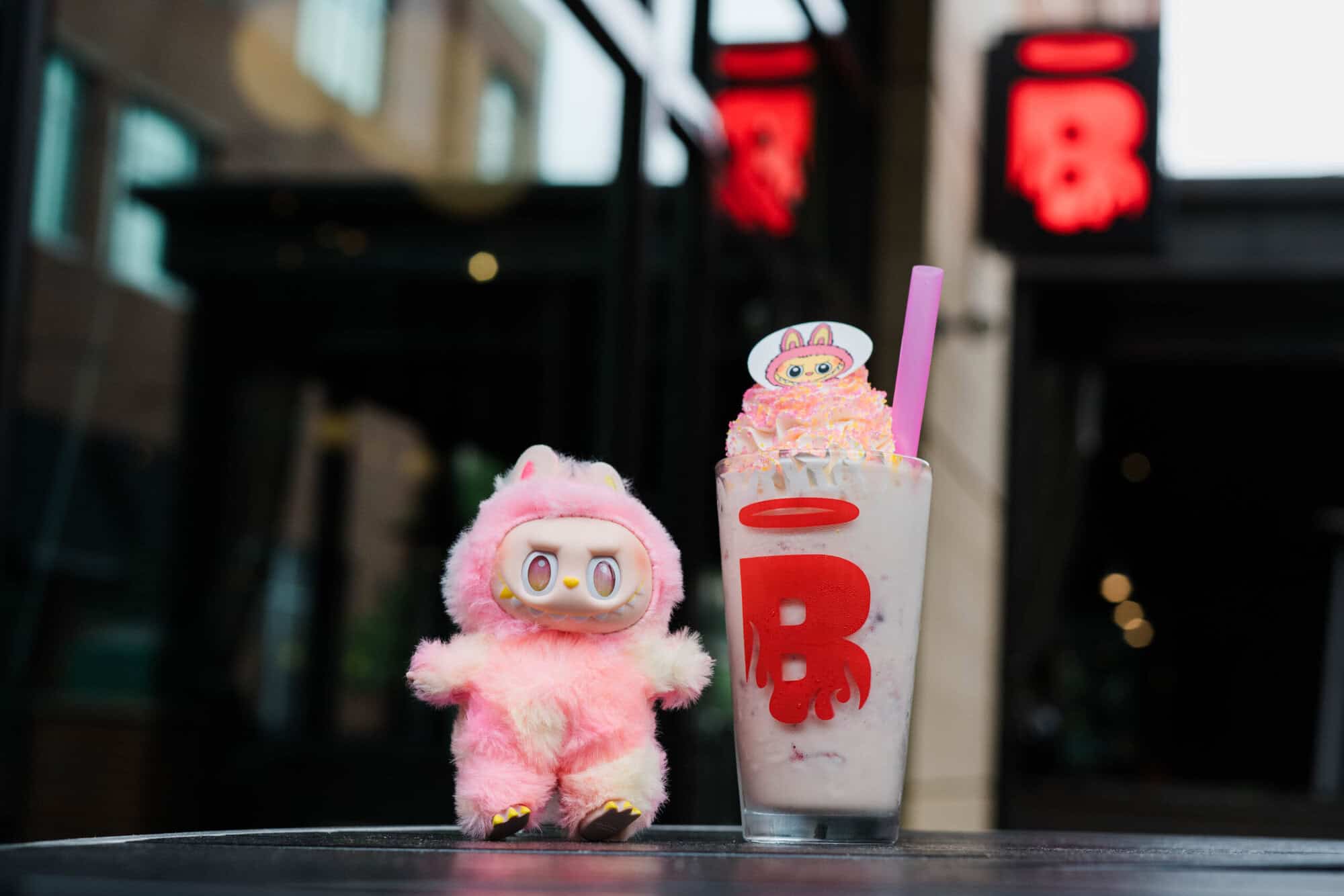 A photo of a Labubu Berry milkshake next to a Labubu toy outside at Burgatory.