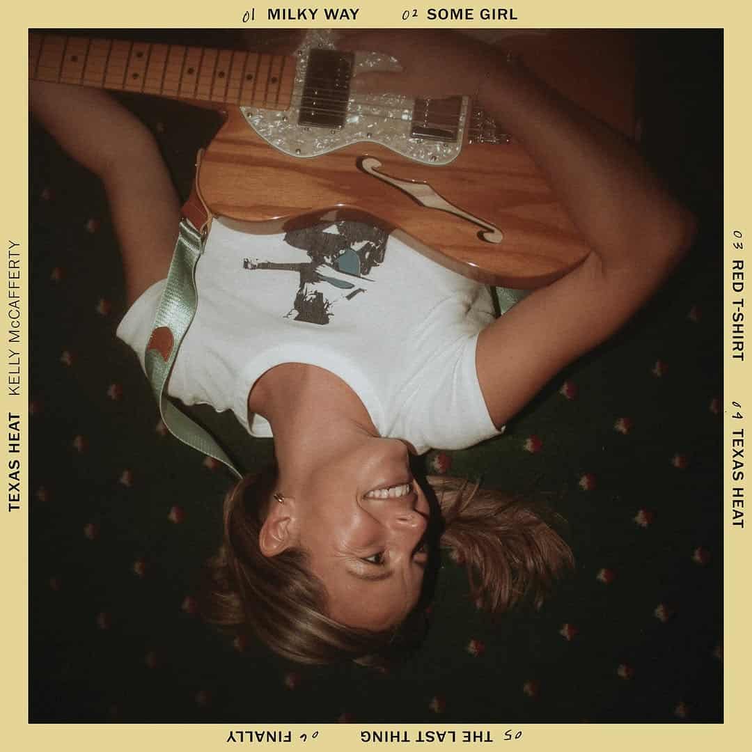 A photo of the back cover of Texas Heat, an EP by Kelly McCafferty. The cover features an upside down photo of Kelly laying down with a guitar, surrounded by a yellow border with song titles.