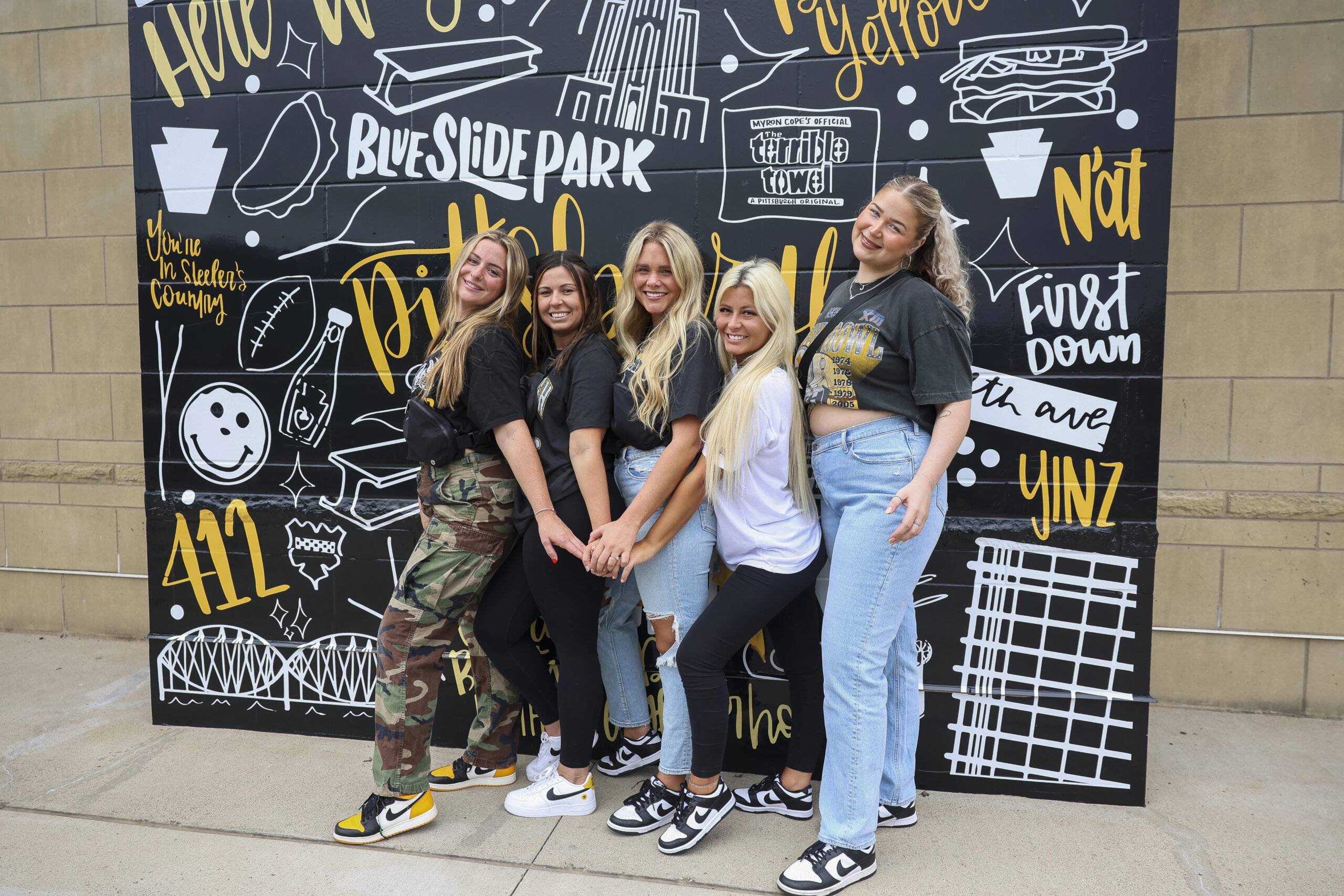 A photo of college students posing in front of a Steelers and Pittsburgh themed backdrop.