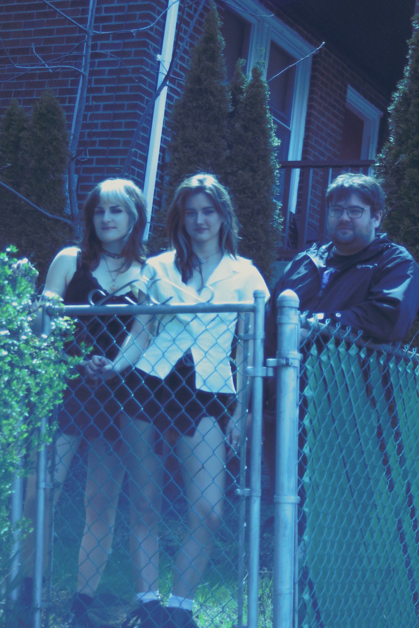 A photo of the three members of Eyewash behind a fence at a house.