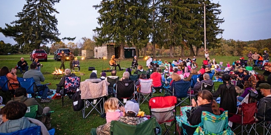A photo of people sitting outside in lawn chairs for Campfire Ghost Stories at a park.